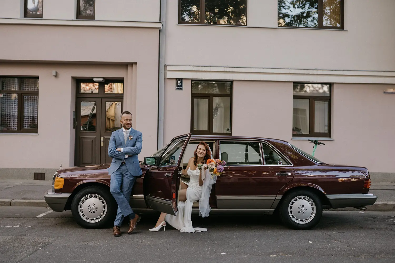 1987. gada Mercedes-Benz 300SDL limuzīns kāzu transporta vizualizācijā. Attēlā redzams elegants, ķiršu sarkans retro limuzīns kopā ar līgavu un līgavaini.